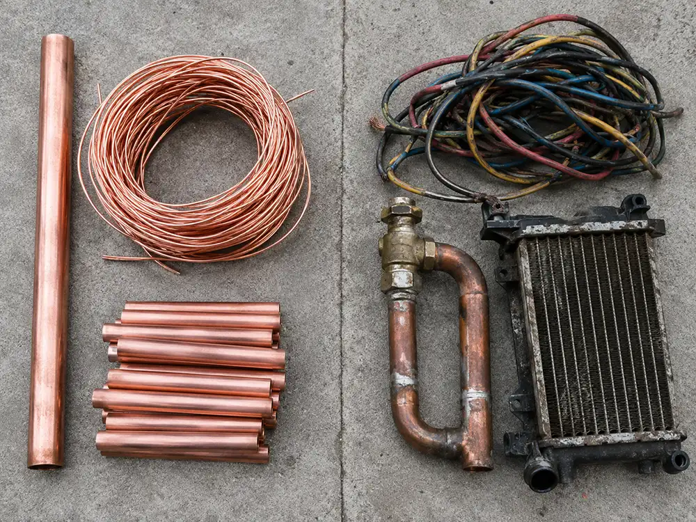 Clean bright copper pipe and stripped wire beside dirty copper with insulation, fittings, and a radiator, showing the difference in scrap grades