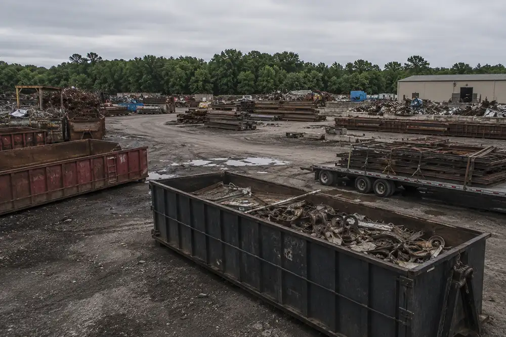 A working North Alabama scrap yard with roll-off containers, a flatbed trailer, and sorted steel, serving contractors, plants, farms, and utilities