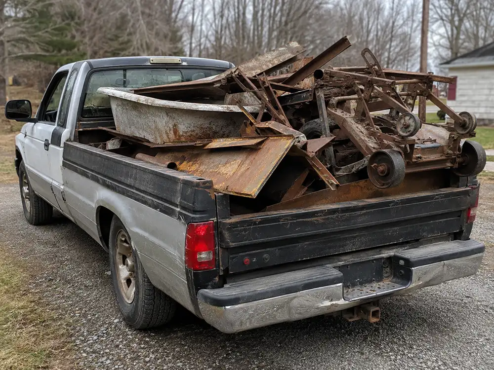 Pickup truck bed loaded heavy with steel and iron scrap, an old bathtub, plate steel, and a mower frame, showing how steel adds up by weight